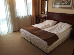 Cama en habitación de hotel con sábanas blancas y manta marrón en Downtown Alexander Services Apartments, en Bansko