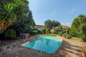 a swimming pool in a yard with trees and a house at Su Casa - Stylish & Spacious Guesthouse in Roodepoort