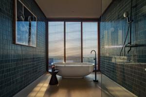 a bathroom with a tub and a large window at Grün Resort Uluwatu in Uluwatu