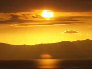 a sunset over the ocean with mountains in the background at Grafton Cottage & Chalets in Thames