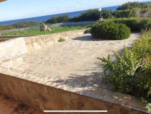 a stone walkway with a stone wall and some bushes at La Pelosa House 2 in Stintino