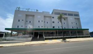 a large white building with a palm tree in front of it at Hotel Greenville by Slim Hotéis in Primavera do Leste