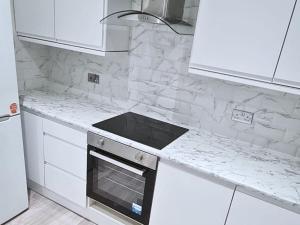 eine weiße Küche mit einem Herd und weißen Schränken in der Unterkunft Modern Penge East Apartment in Sydenham