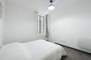 a white bedroom with a bed and a window at T2 apartment in the heart of Cuxac-d'Aude in Cuxac-dʼAude
