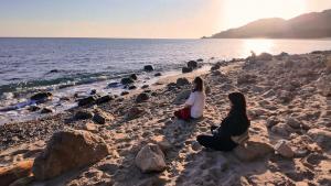 two women sitting on a beach near the water at WakeTheFUP Holistic Meditation Temple in Mas Boquera