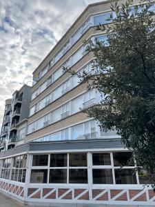 een hoog wit gebouw met ramen en een boom bij Zonnige studio Mermoz Koksijde-Bad in Koksijde
