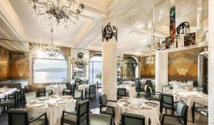 a restaurant with white tables and chairs and a chandelier at Hôtel Belles Rives in Juan-les-Pins