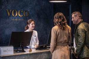 two women and a man standing at a desk with a computer at voco Auckland City Centre by IHG in Auckland