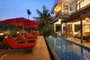 a house with a swimming pool with red chairs and umbrellas at The Magic Villa Keramas in Gianyar