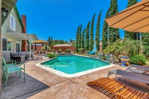 Una piscina en un patio con sillas y una sombrilla. en Tropical Bliss - 5BR Pool Spa Games 12 min to dwtn, en San Diego
