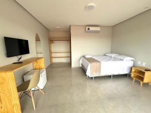a bedroom with a bed and a desk with a television at Encanto da Barra Pousada in Barra Grande