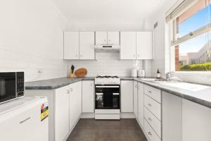 Una cocina blanca con gabinetes blancos y una ventana. en The Sunlit Fern - Minutes from Dining & Coastline, en Sídney