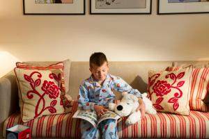 
a boy sitting on a couch reading a book at Rocco Forte Hotel Amigo in Brussels

