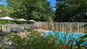 a pool with chairs and umbrellas next to a fence at chalet Vital avec Spa privatif in Biron