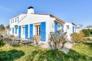 a white house with blue shutters and chairs at Maison pour 7 à 900m de la plage avec jardin in Barbâtre
