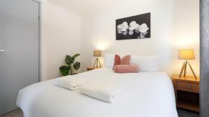 a bedroom with a white bed with white sheets and pink pillows at Heights Hideaway in Kiama