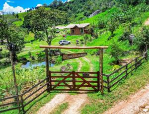 a gate in a field with a house on a hill at Chalé Jacarandá - Hidro - Wifi e mais in Sapucaí-Mirim