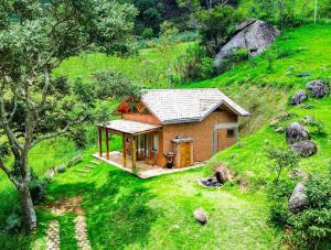a small house sitting on top of a green hill at Chalé Jacarandá - Hidro - Wifi e mais in Sapucaí-Mirim