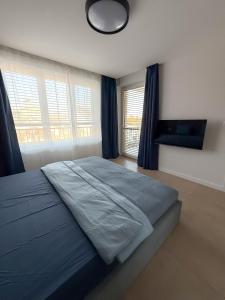 a bedroom with a large bed with blue sheets and windows at Urban Nest Apartment in Dunajská Streda