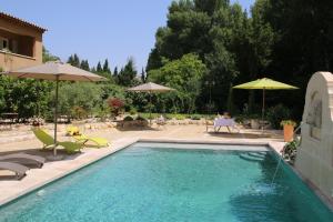 a swimming pool with chairs and umbrellas in a yard at La Bastide des Cyprès in Maussane-les-Alpilles