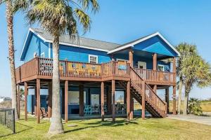 a blue house with a deck and palm trees at Caribbean Palm 3BR Retreat King Bed Fireplace in Bolivar Peninsula