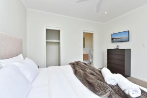 a white bedroom with a large white bed and a tv at Beach Escape at Caves Beach Villas in Caves Beach +32 photos