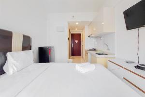 a white bedroom with a large bed and a kitchen at Cozy Style Studio Room at High Floor Sky House BSD Apartment By Travelio in Tangerang +8 photos