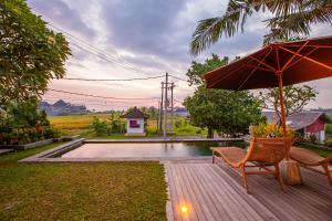 a patio with an umbrella and chairs and a pool at Jero Kelodan Villa in Tabanan