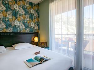 a bedroom with a bed with a book and glasses at ibis Styles Beaulieu sur Mer in Beaulieu-sur-Mer