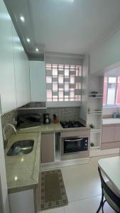 a white kitchen with a sink and a stove at Apto Charmoso Próximo à Catedral in Santa Cruz do Sul