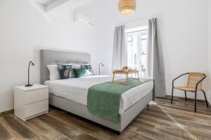 a white bedroom with a bed and a chair at Roots Apartments in Faro