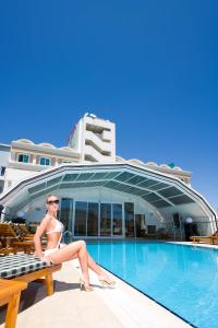 a woman sitting on a bench next to a swimming pool at Latanya Palm Hotel Antalya in Antalya
