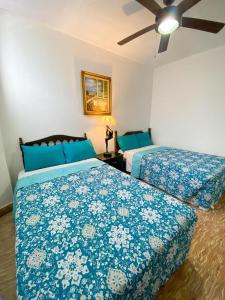 Un dormitorio con dos camas con sábanas azules y un ventilador. en Hostal VELVET PLAZA, en Santa Ana