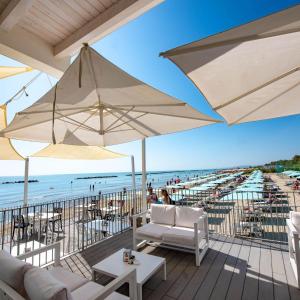 a patio with white chairs and an umbrella on the beach at Villaggio Camping Duca Amedeo in Martinsicuro