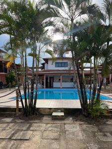 a pool with palm trees in front of a house at Pousada Lorenise in Guriri +10 photos