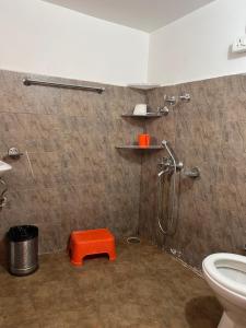 a bathroom with a shower and a toilet with an orange stool at Brahma Cottages in Kasol