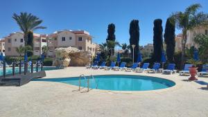 a swimming pool with blue chairs and palm trees at Pyla Village Resort E108 in Pyla