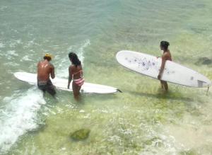 three people are standing in the water with their surfboards at Surfer's Paradise Retreat - Gated Community Townhouse for Surfers & Families in Christ Church