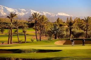 a golf course with palm trees and mountains in the background at La Perle de l'Atlas by Golf Resort in Marrakesh