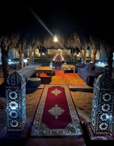 a room with a red carpet and tables and lights at Merzouga Beduien Camping in Merzouga
