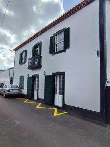a white building with green shuttered windows and a car at Casa da Praça I in Vila Nova