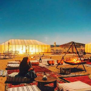 a woman sitting on a blanket in front of a tent at Merzouga Beduien Camping in Merzouga