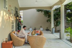 a man sitting in wicker chairs on a porch at SaffronStays Mont Tierra - 4BR modern villa with lawn, bonfire, indoor games & themed rooms, Dehradun in Dehradun