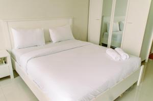 a white bed with white pillows and a mirror at Comfort and Homey Studio at Parkland Avenue Apartment By Travelio in Tangerang +12 photos