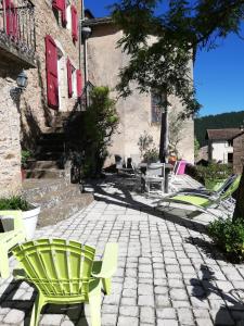 Un patio de piedra con sillas verdes y un edificio. en Maison de caractère au cœur des grands causses, en Viala-du-Tarn