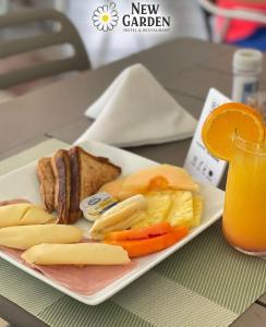 a plate of food with cheese and fruit and a glass of orange juice at New Garden Hotel in Sosúa