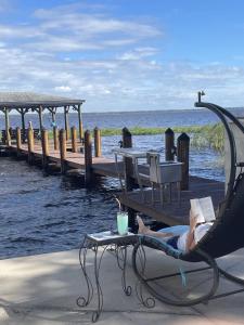 a woman laying in a chair reading a book next to a dock at The Lake House on Lake Rosalie in Lake Wales