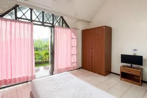 a bedroom with a bed and a tv and a window at Urbanview Hotel AR Cottage Gambung in Gambung