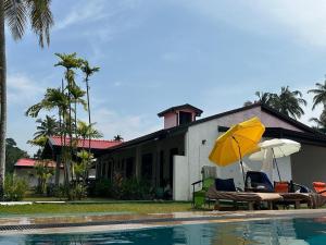 a house with chairs and an umbrella next to a swimming pool at Neos Palm Paradise in Aluthgama