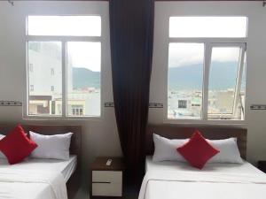 two beds with red pillows in a room with two windows at LUXURY Motel in Danang